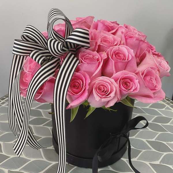 Pink roses in a black hatbox with a black-and-white striped ribbon