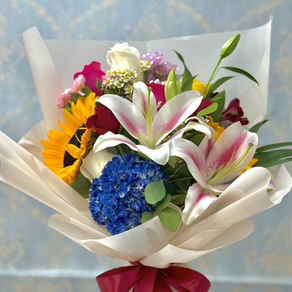 Mixed bouquet with lilies, sunflowers, roses, and hydrangea wrapped in white paper