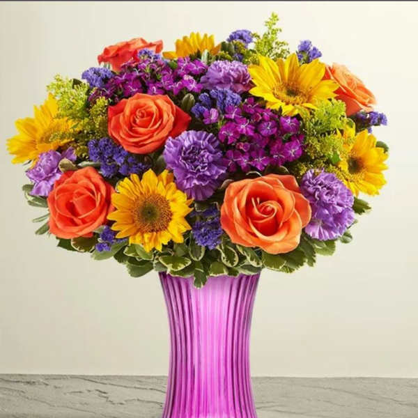 Colorful bouquet of roses, sunflowers, and purple flowers in a pink vase