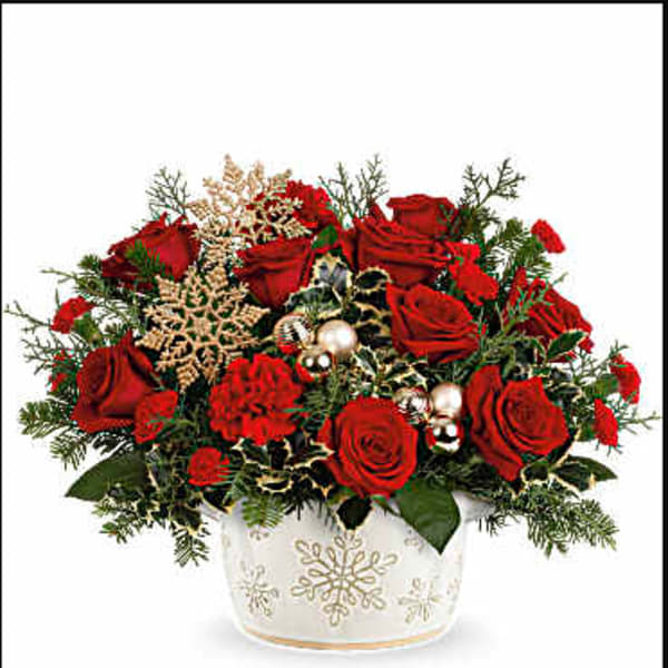 Red roses arranged in a white snowflake vase with holiday accents