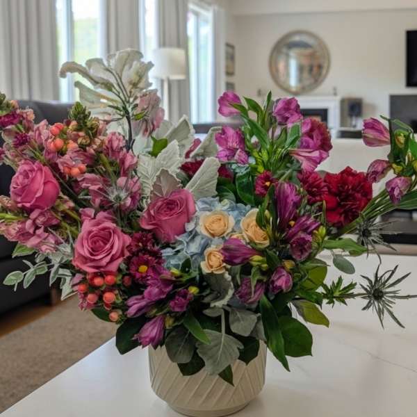 Mixed bouquet of pink and purple flowers in a cream vase
