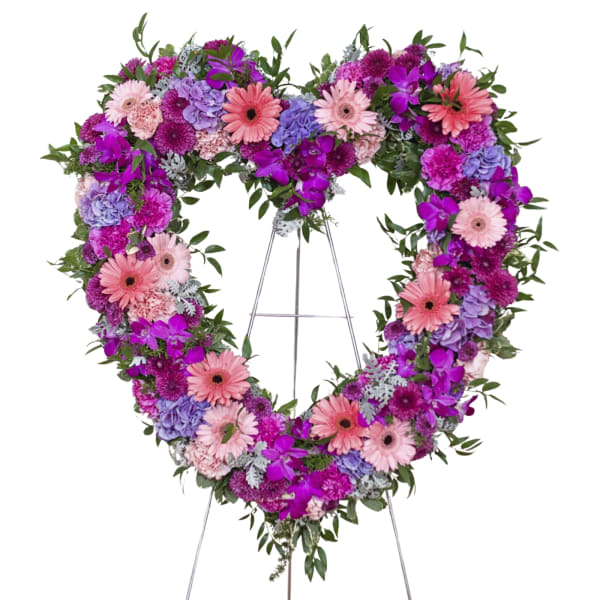 Heart-shaped floral wreath on a stand with pink, purple, and lavender blooms