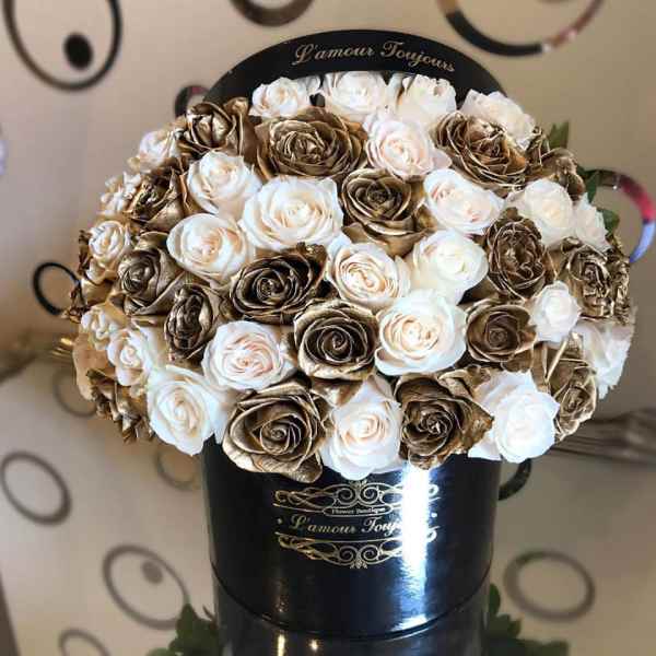 Round box of white and gold roses arranged tightly in a black hatbox-style container