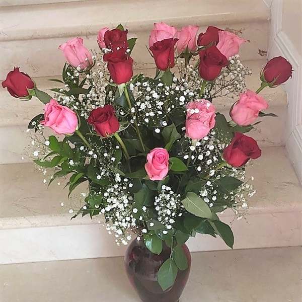 Tall arrangement of red and pink roses with white filler flowers in a dark vase