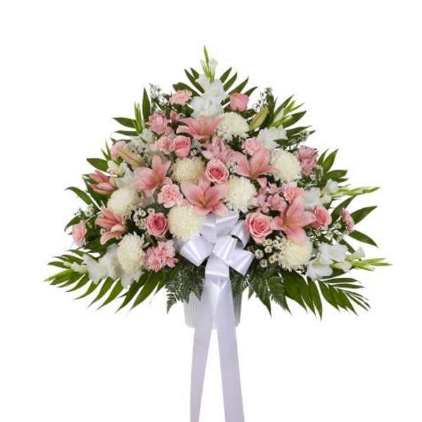 Fan-shaped standing arrangement of pink lilies, roses, and white mums with a white bow.