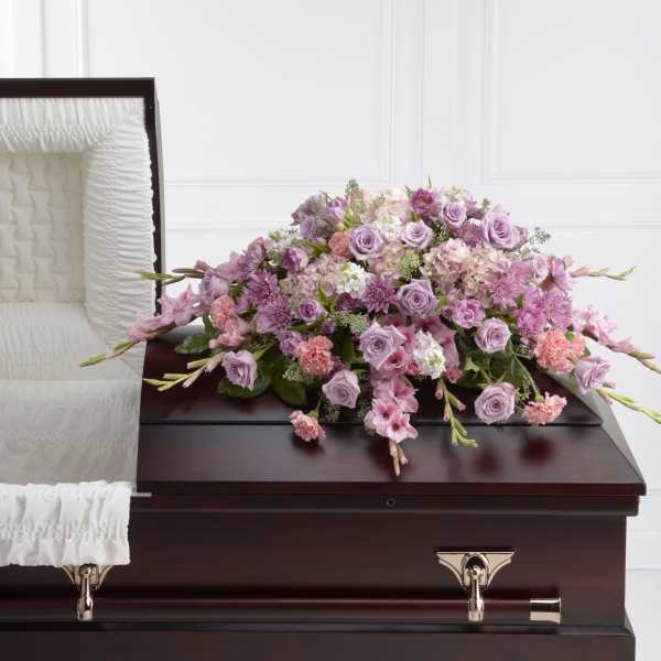 Lavender and pink casket spray of roses and mixed flowers on a dark wood casket