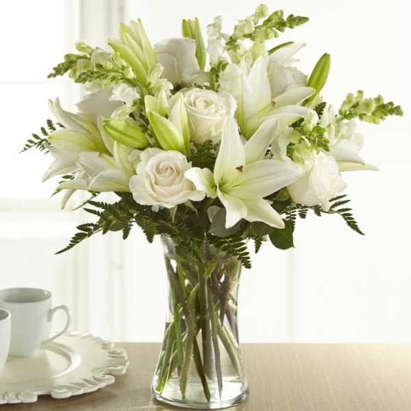 White lilies, roses, and snapdragons arranged in a clear glass vase.