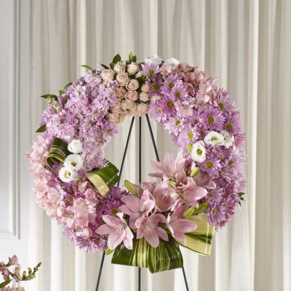 Large pink floral wreath with lilies, roses, and mums on a black metal stand