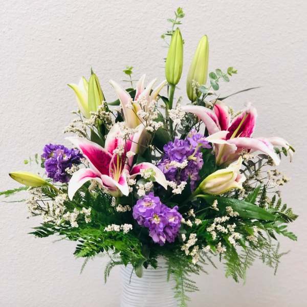 Pink lilies and purple flowers in a white vase with fern accents