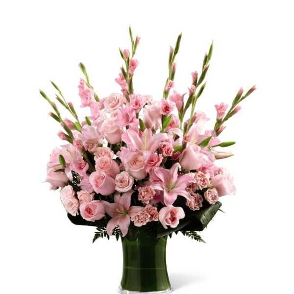 Tall pink bouquet of lilies, roses, and carnations in a green-wrapped glass vase