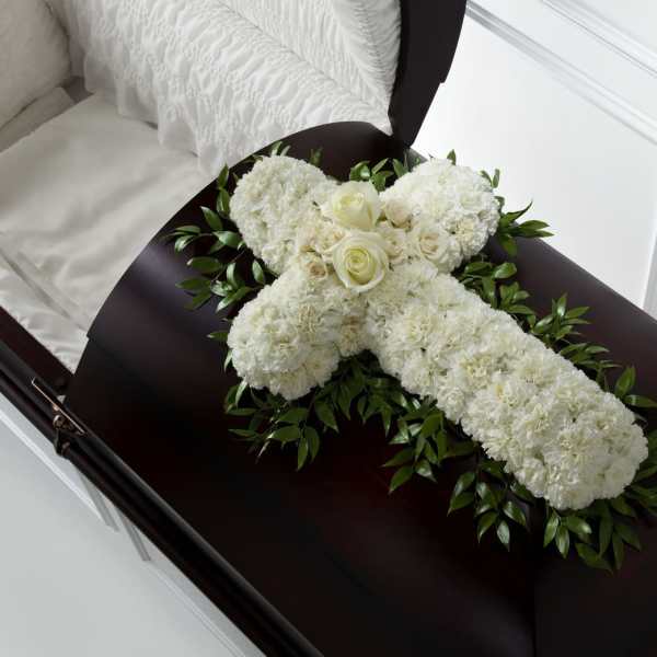 White floral cross with cream roses resting on a dark wood casket.