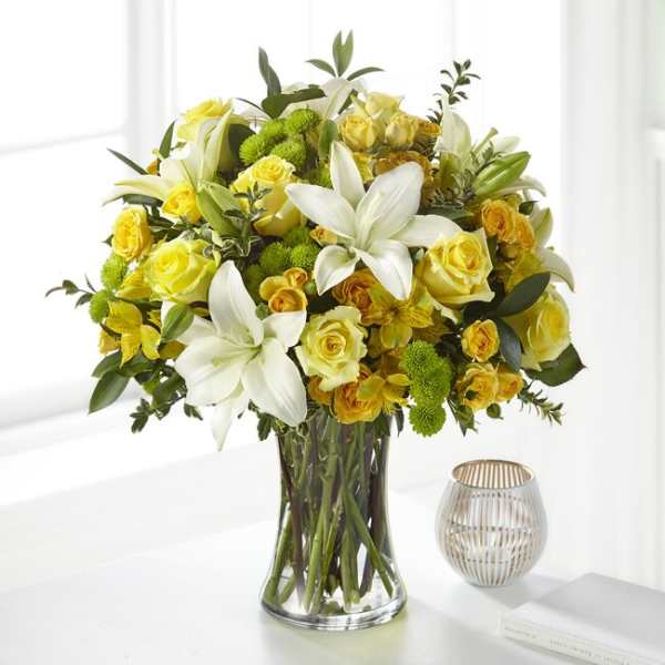 Yellow roses and white lilies arranged in a clear glass vase