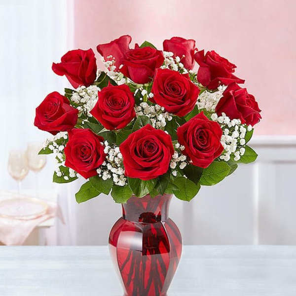 Red roses arranged in a red glass vase with white filler flowers