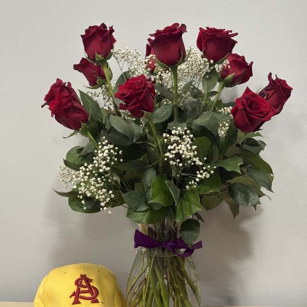 Bouquet of red roses in a glass vase with a yellow cap beside it.