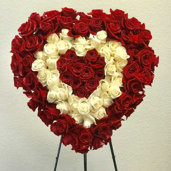 Heart-shaped standing arrangement of red and white roses on a black easel.