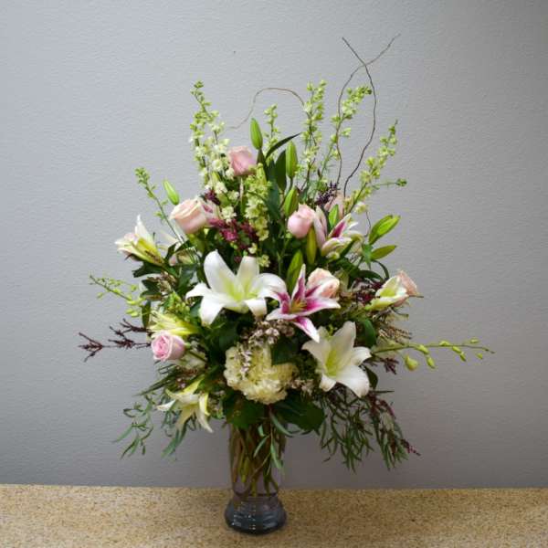 Tall arrangement of white lilies and pale pink roses in a clear glass vase