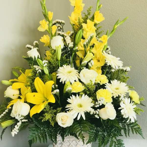 Tall yellow and white flower arrangement with lilies, roses, and daisies in a white woven basket