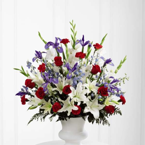 Tall red, white, and purple arrangement with lilies, roses, and irises in a white urn vase