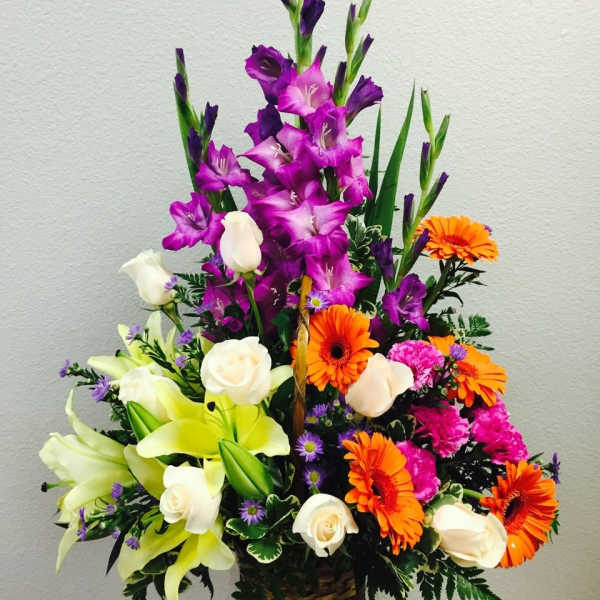 Tall mixed arrangement with purple flowers, orange gerberas, white roses, and yellow lilies in a basket