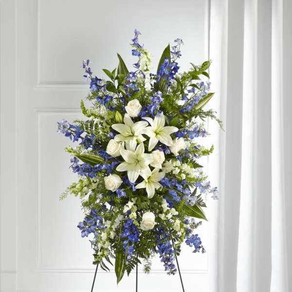 Tall standing floral spray with white lilies, white roses, and blue flowers