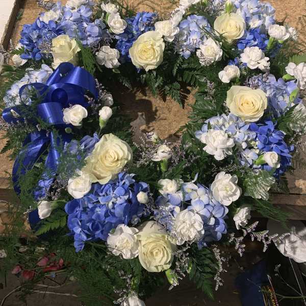 Blue and white floral wreath with cream roses and a blue ribbon