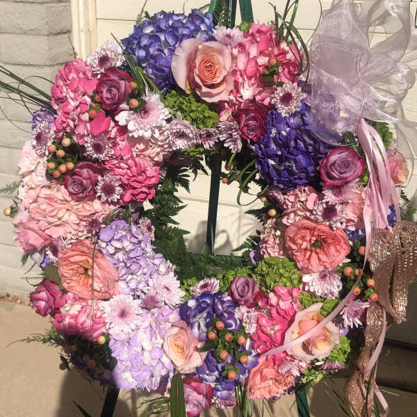 Colorful floral wreath with roses, hydrangeas, and ribbon on a stand