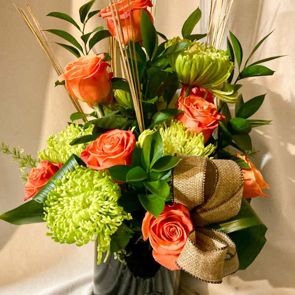 Orange roses and green chrysanthemums in a black vase with a gold ribbon