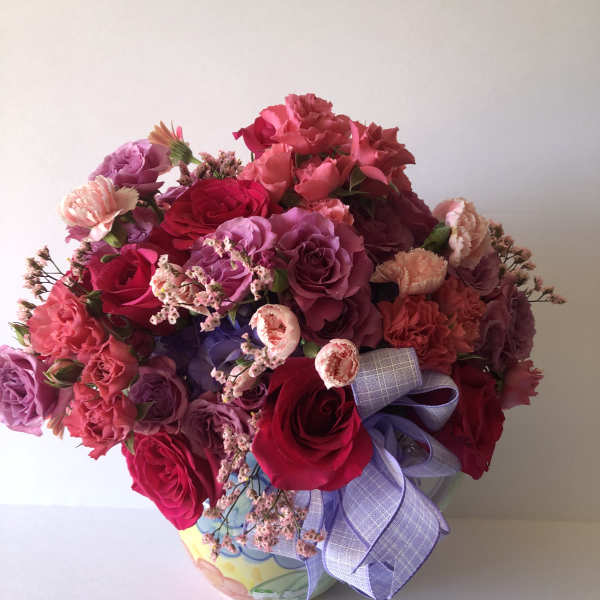 Bouquet of pink and purple roses in a decorative vase with a lavender ribbon