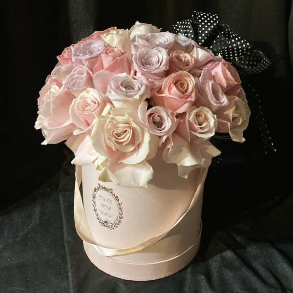 Pink and white roses arranged in a round hat box with a black polka-dot ribbon