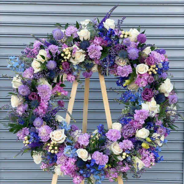 Large circular wreath of purple, blue, and white flowers on a wooden easel