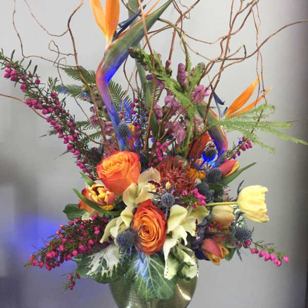 Tall mixed flower arrangement in a glass vase with orange and yellow blooms