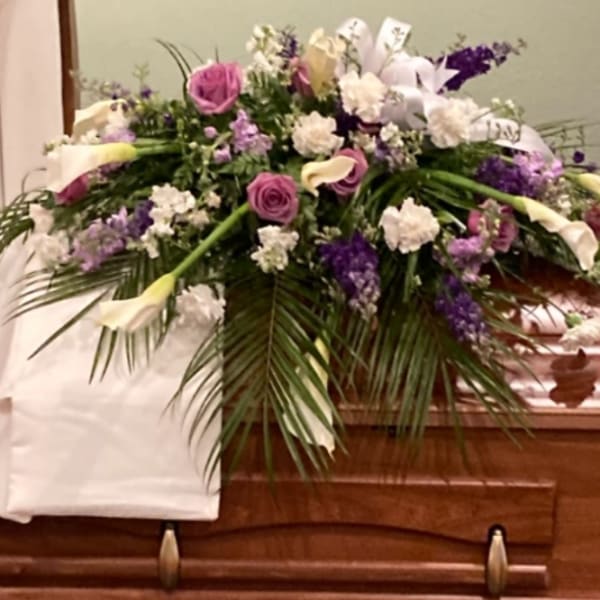 Floral casket spray with pink roses, white lilies, and purple flowers