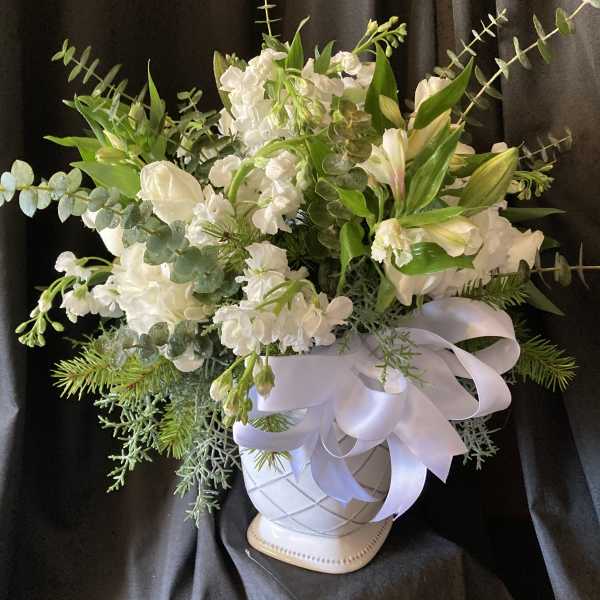White floral arrangement in a white vase with a satin ribbon