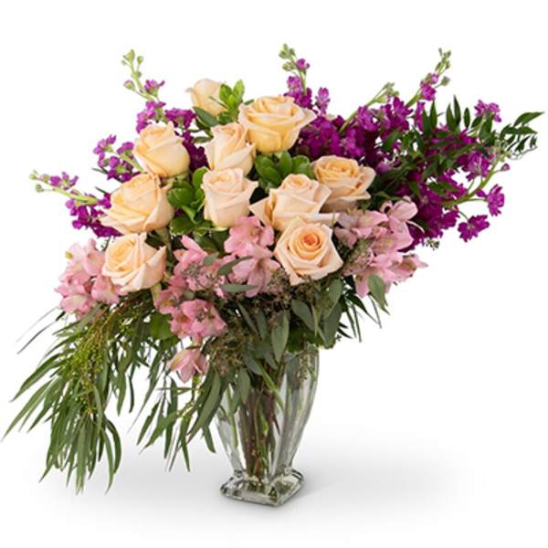 Peach roses and purple flowers in a clear glass vase