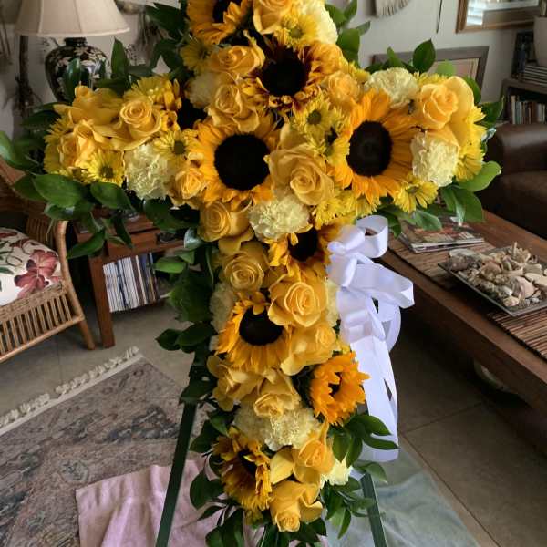 Tall yellow floral standing spray with sunflowers, roses, and a white ribbon