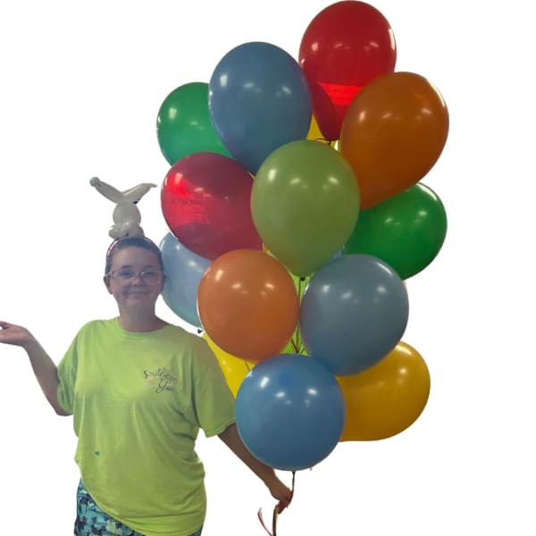 Person holding a bunch of colorful balloons with a small balloon animal on her head