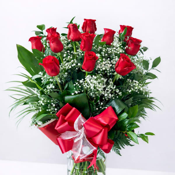 Red roses arranged in a clear glass vase with a red ribbon bow