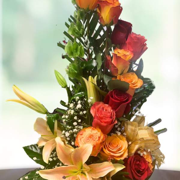 Tall bouquet of orange and red roses with lilies in a vase