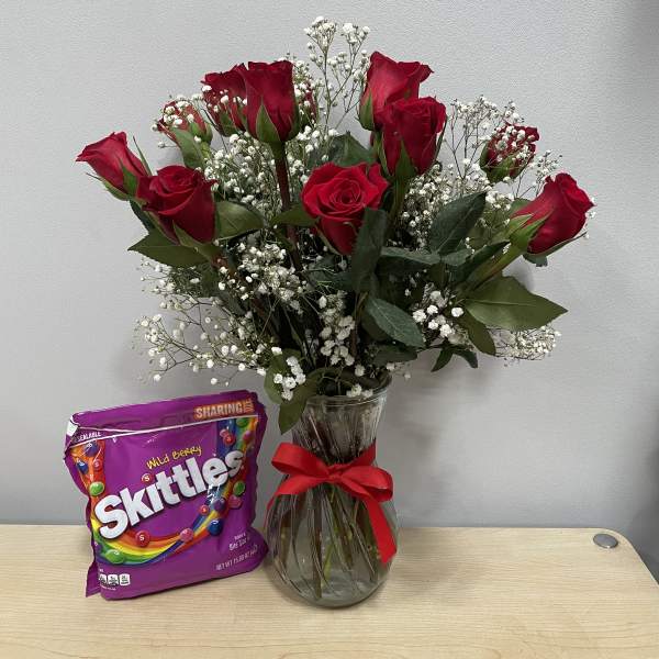 Red roses in a glass vase with a bag of Skittles candy
