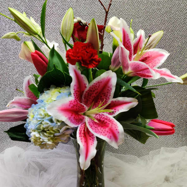 Bouquet of pink lilies, hydrangea, and red carnations in a glass vase