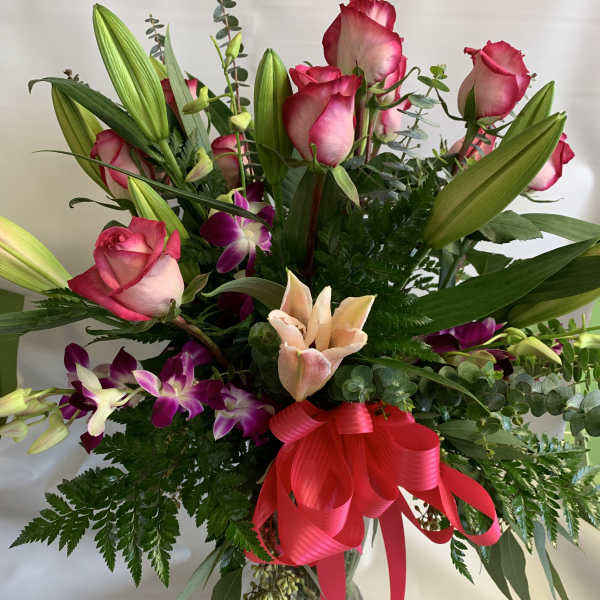 Bouquet of pink roses, lilies, and purple orchids in a glass vase