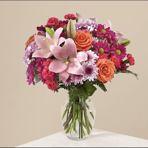 Bouquet of pink lilies, orange roses, and purple daisies in a glass vase