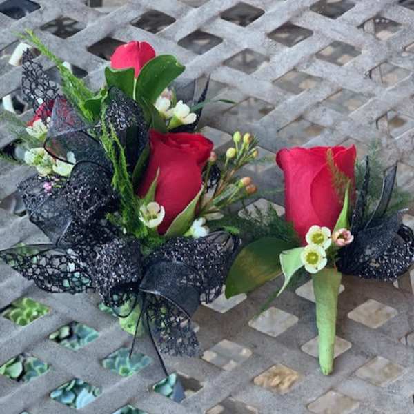 Two red rose boutonnieres with black ribbon accents on a metal table