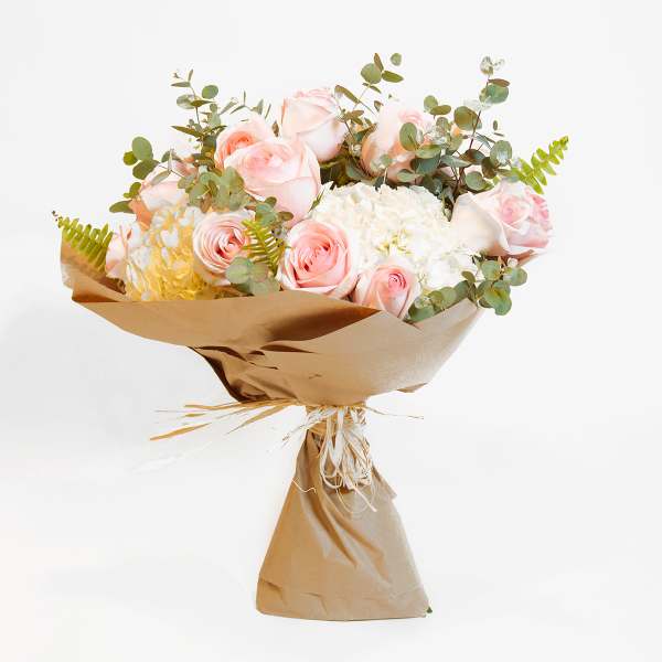 Bouquet of pale pink roses and white hydrangeas wrapped in brown paper