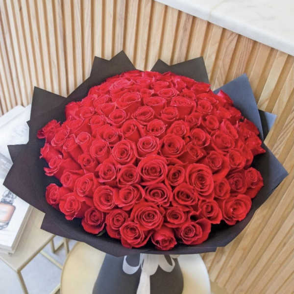 Large bouquet of tightly clustered red roses wrapped in black paper and tied with a white ribbon