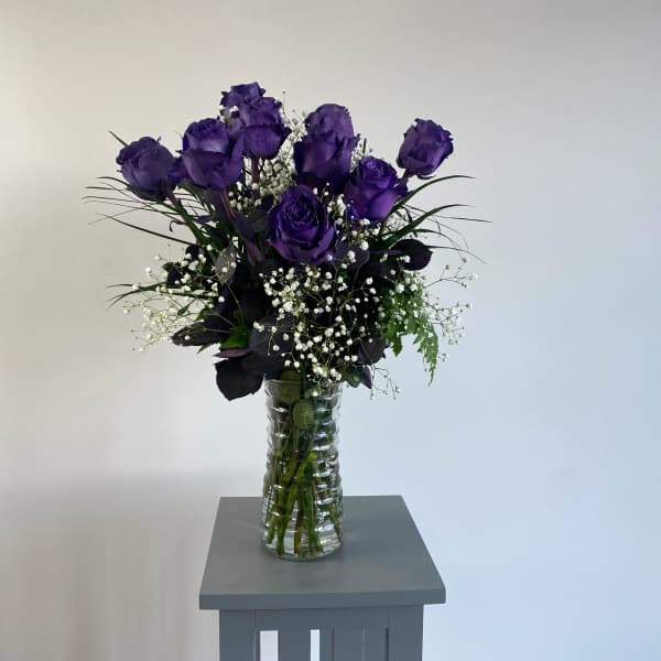 Purple roses in a clear glass vase with white baby's breath