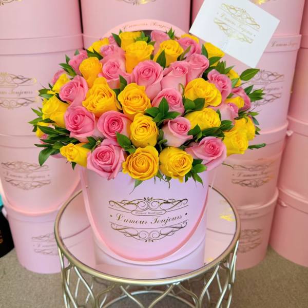 Pink and yellow roses arranged in a round pink hat box