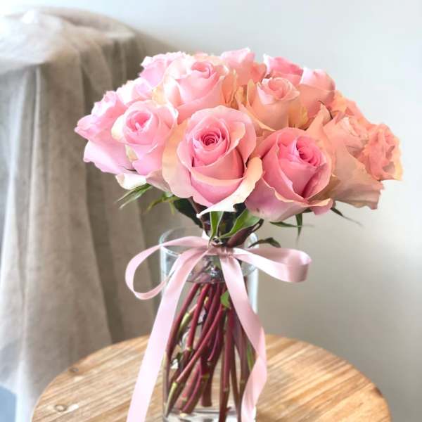 Pink rose bouquet in a clear glass vase with a pink ribbon