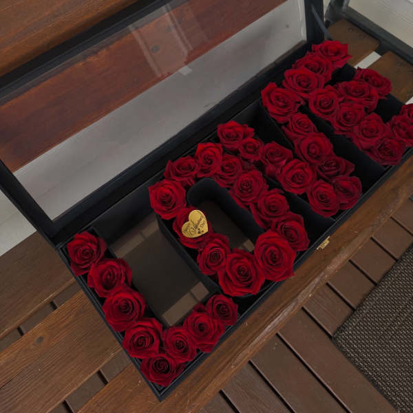 Red roses arranged in a black gift box to form letters.