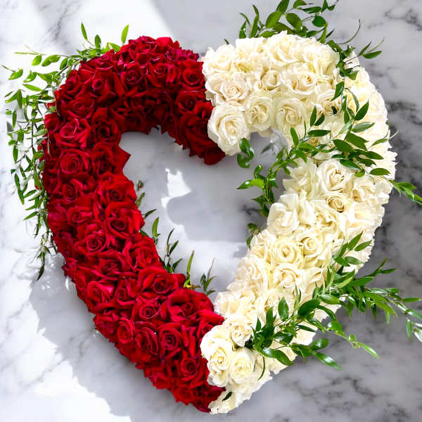 Heart-shaped arrangement of red and white roses with greenery